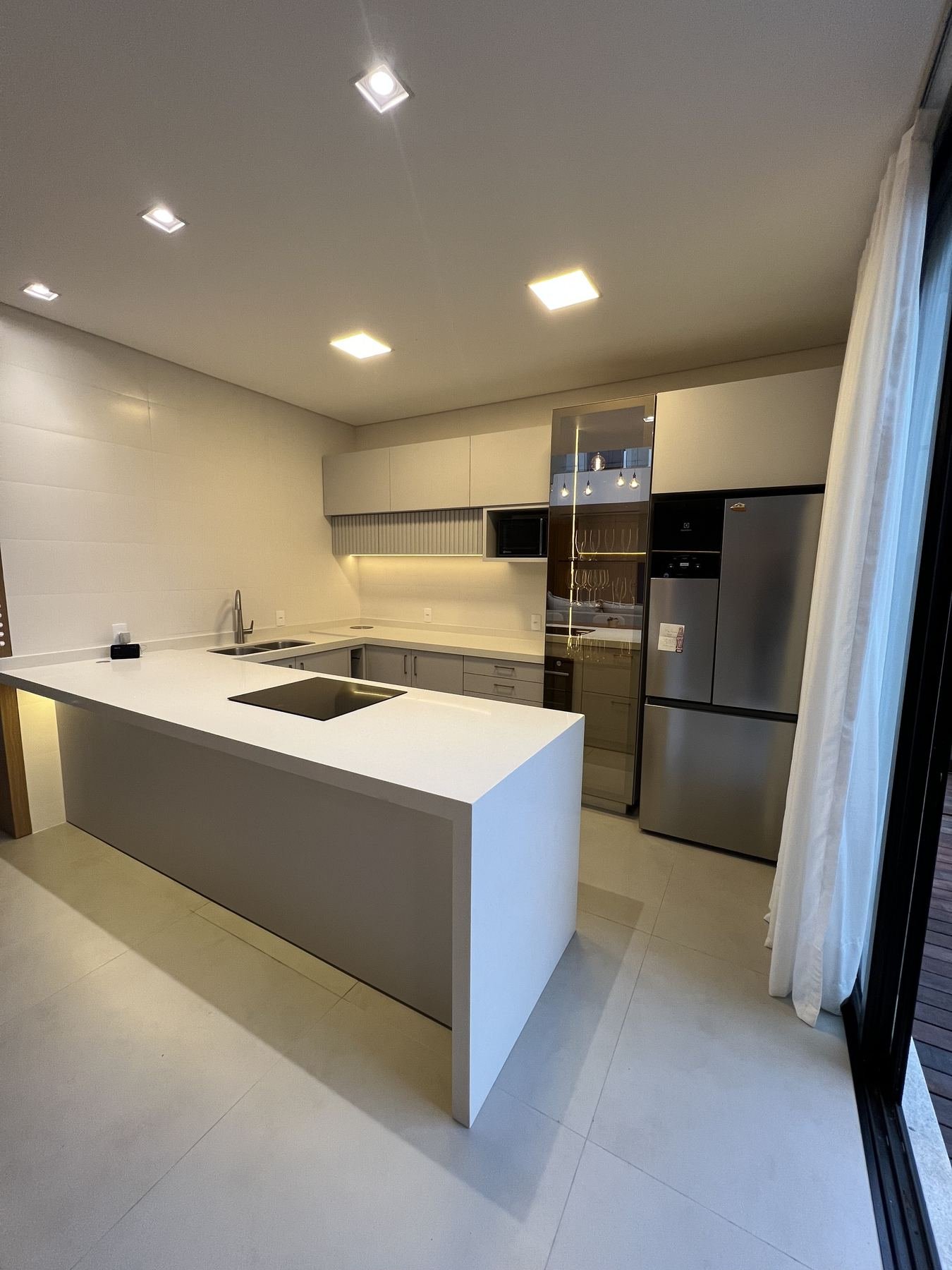 Cozinha planejada com adega de vidro, iluminação embutida e cortina